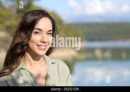 Donna felice che guarda la macchina fotografica in posa in un lago Foto Stock