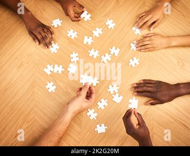 Presto avrà tutti senso. Scatto ritagliato di un gruppo di uomini d'affari che completano un puzzle insieme su un tavolo. Foto Stock