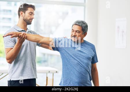 Allungati per me. Scatto corto di un giovane fisioterapista maschile che assiste un paziente anziano in guarigione. Foto Stock