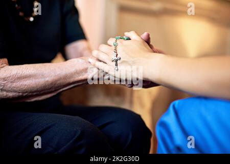 Se avete bisogno di una preghiera, sappiate che im qui. Scatto ritagliato di una persona che tiene compassionately un rosario e le mani di un anziano womans. Foto Stock