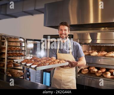 Appena sfornato, solo per voi. Scatto corto di un uomo che tira fuori un lotto fresco di croissant da servire ai suoi clienti. Foto Stock