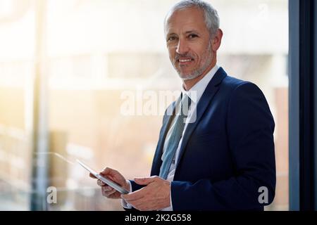 Restare al passo con le tendenze aziendali digitali. Ritratto di un uomo d'affari maturo sorridente che usa un tablet digitale mentre si trova in ufficio. Foto Stock