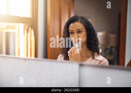 L'igiene orale è importante per lei. Scatto corto di una giovane donna attraente spazzolando i denti nel bagno di casa. Foto Stock