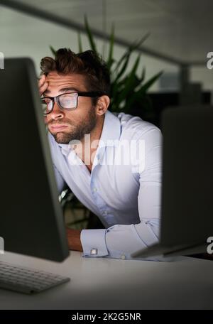 Mettendo nelle ore per realizzare il successo. Shot di un giovane uomo d'affari che lavora tardi in ufficio. Foto Stock