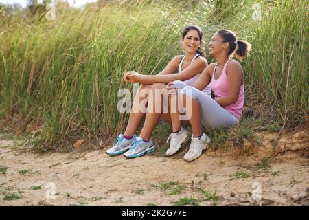 Condividere uno scherzo tra amici. Due amici seduti all'aperto ridendo insieme indossando abiti da ginnastica. Foto Stock