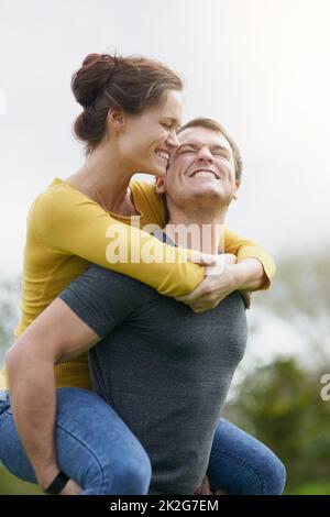 L'amore fa il tempo per il divertimento. Scatto di un uomo felice che dà a sua moglie un giro di piggyback fuori. Foto Stock