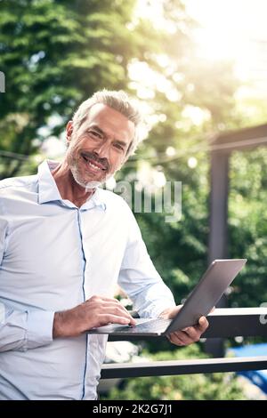 È un buon giorno per fare affari. Ritratto di un uomo d'affari maturo che utilizza un notebook all'esterno. Foto Stock