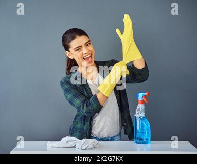 Non pulisco mai senza i miei guanti di gomma. Ritratto di studio di una giovane donna attraente che mette sui suoi guanti di gomma per fare una certa pulizia della molla. Foto Stock