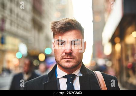 Solo un altro uomo che vive in città. Ritratto di un giovane uomo d'affari fiducioso in piedi nel mezzo delle strade trafficate della città durante le ore del mattino. Foto Stock