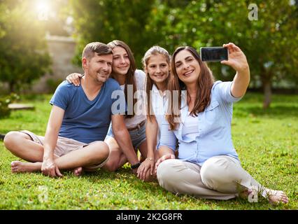 Questo è per i nonni. Foto di una famiglia allegra seduta in un parco mentre si prende un autoritratto insieme fuori durante il giorno. Foto Stock