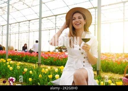 Donna di bellezza rilassata tiene calice di vino tra tulipani in serra Foto Stock