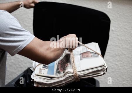 Fare la mia parte per salvare l'ambiente. Colpo di un giovane uomo che mette il giornale nel bidone per essere riciclato. Foto Stock