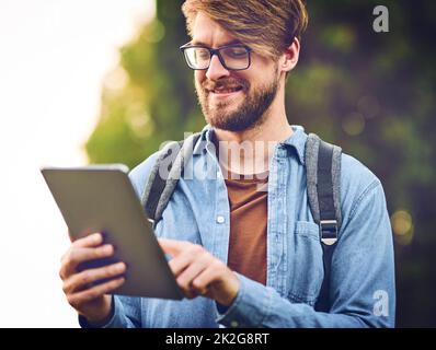 Rimani connesso anche in natura. Scatto corto di un bel giovane uomo usando un tablet all'aperto. Foto Stock