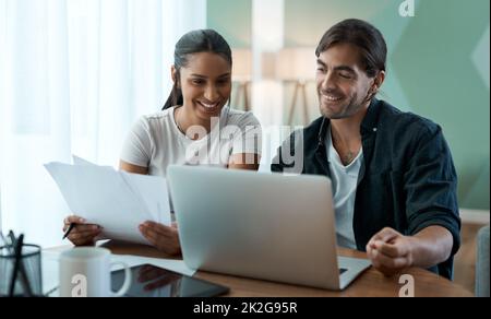 Facciamo un buon team. Scatto di una giovane coppia che fa la documentazione mentre usa un laptop a casa. Foto Stock