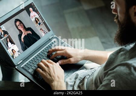 Intervista online. Video riunione. Conferenza digitale. Uomo rilassato che utilizza un notebook lavorando con il team aziendale sullo schermo dell'ufficio virtuale con spazio libero. Foto Stock