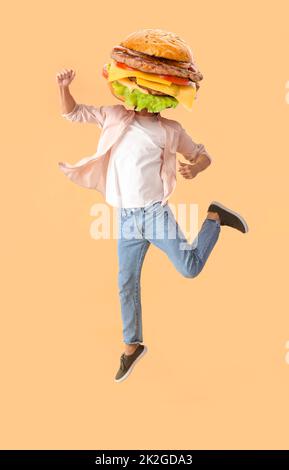 Saltando l'uomo con gustoso hamburger invece della sua testa su sfondo beige Foto Stock