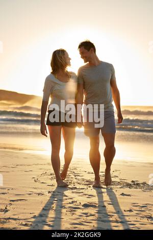 Im così felice che posso appoggiarmi su di lui. Scatto di una coppia che cammina vicino insieme sulla spiaggia al tramonto. Foto Stock