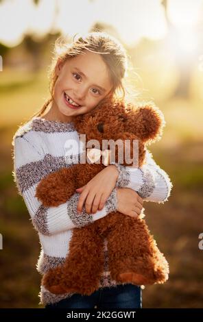 Teddy è il suo primo vero amore. Ritratto di una bambina dolce che abbraccia il suo orsacchiotto mentre gioca all'esterno. Foto Stock