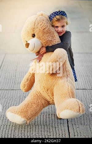 Più grande è l'orso, più grandi sono le cuddle. Ritratto di una ragazza carina che tiene un orsacchiotto enorme mentre gioca all'esterno. Foto Stock