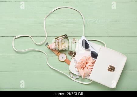 Borsa femmina aperta con diversi accessori su fondo in legno verde Foto Stock