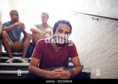 Raffreddare con i ragazzi nella scala. Ritratto di uno studente universitario maschio seduto con i suoi amici sui gradini di una scala. Foto Stock