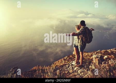 Lascia volare via insieme. Scatto di una giovane coppia avventurosa ammirando la vista da una cima di montagna mentre fuori in un'escursione. Foto Stock
