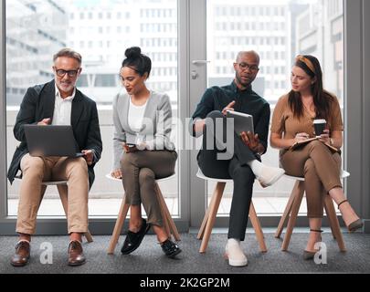 Scelte per il futuro. Girato di un gruppo di uomini d'affari che utilizzano i loro dispositivi elettronici su uno sfondo di vetro in città. Foto Stock