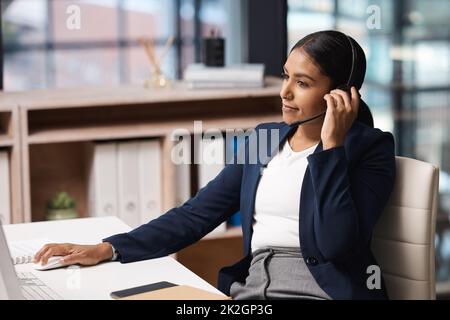 Assumere il suo ruolo di agente efficiente. Scatto di una giovane donna d'affari che lavora su un computer in un call center. Foto Stock