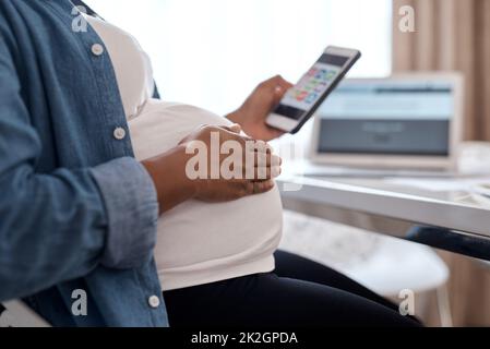 Questa app mi ha aiutato molto nel mio viaggio di gravidanza. Scatto corto di una donna incinta usando il suo cellulare mentre si siede a casa. Foto Stock