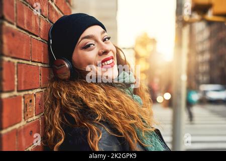 La musica è la migliore terapia. Scatto corto di una giovane donna che ascolta la musica mentre si appoggia contro una parete di mattoni all'esterno. Foto Stock