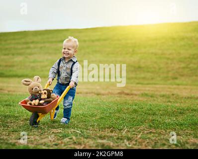 Piccole avventure in una grande fattoria. Shot di un adorabile ragazzino che spinge una carriola giocattolo piena di animali imbalsamati in una fattoria. Foto Stock