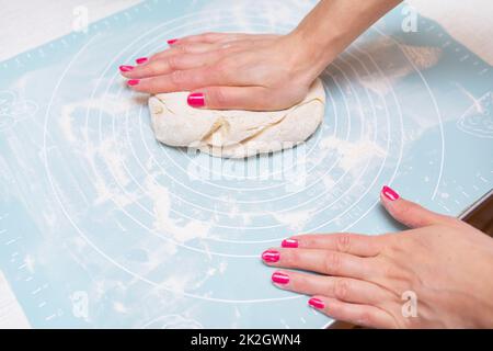 Preparazione dell'impasto, cottura a casa. Le mani femminili stendono l'impasto su un tappetino in silicone. Foto Stock