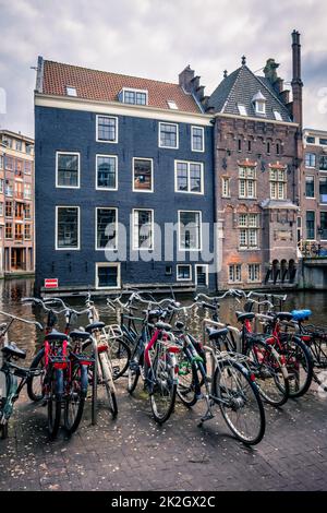 Biciclette in Amsterdam street vicino a canal con vecchie case Foto Stock