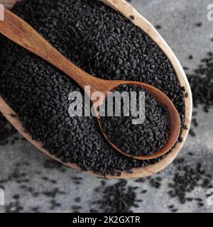 Spezie indiane cumino nero (nigella sativa o kalonji) semi in ciotola con cucchiaio su tavola di legno vista dall'alto. Foto Stock