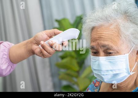 Caregiver che tiene termometro digitale per misurare asiatico anziano o anziano donna anziana paziente che indossa una maschera viso hanno una febbre in ospedale, sano forte concetto medico. Foto Stock