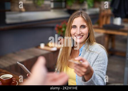 Pagare per il suo acquisto. Scatto corto di una giovane donna che consegna a qualcuno la sua carta di credito per il pagamento in un caffè. Foto Stock