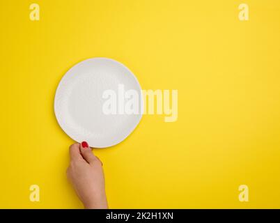 mano femmina che tiene una piastra rotonda vuota bianca su sfondo giallo, vista dall'alto Foto Stock