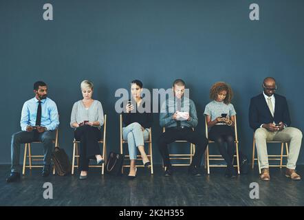 Potrebbe essere chiunque di noi. Shot di un gruppo di uomini d'affari ben vestiti seduti in fila in attesa di essere intervistati. Foto Stock