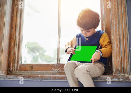 I bambini di questi giorni sono interamente circa la tecnologia. Scatto corto di un ragazzo giovane usando un tablet mentre si siede su un davanzale. Foto Stock