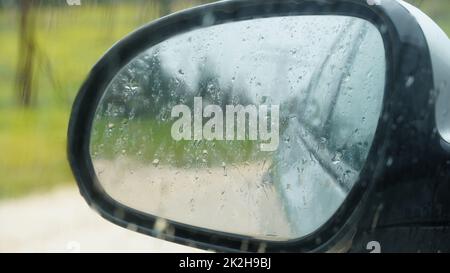 La pioggia sfocata scende sul finestrino di un'auto con lo specchio sullo sfondo. Primo piano Foto Stock