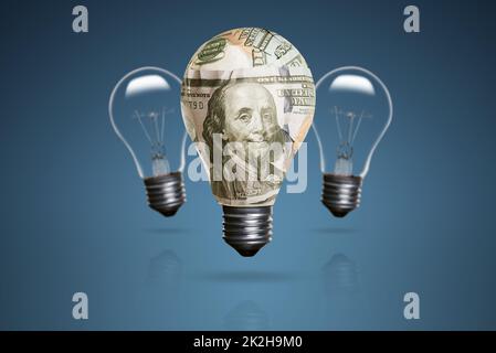 Una lampadina avvolta con circa 100 banconote di dollari e ci sono due lampadine sullo sfondo e su uno sfondo blu. Foto Stock