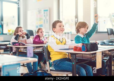 Gli alunni della classe scolastica elementare alzano le mani per rispondere Foto Stock