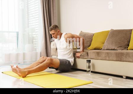 L'uomo che fa i triceps si immerge sul bordo del divano durante l'allenamento domestico Foto Stock