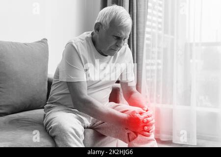 Uomo anziano che soffre di dolore al ginocchio a casa. Foto Stock