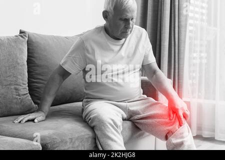 Uomo anziano che soffre di dolore al ginocchio a casa. Foto Stock