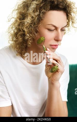 Bella donna che fa il massaggio facciale con un dermaroller di giada a casa Foto Stock