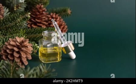 Bottiglia di vetro con contagocce con olio essenziale di conifere vicino a rami di abete e coni di pino su primo piano verde Foto Stock