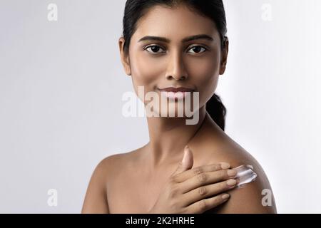 Bella donna indiana che applica crema idratante o crema solare lozione sul suo corpo Foto Stock