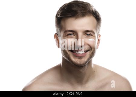 La bellezza degli uomini. Giovane uomo sta applicando crema idratante e anti invecchiamento sul suo viso Foto Stock