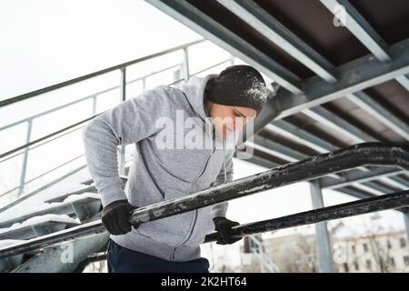 Giovane uomo atletico che fa tuffi su un bar parallelo durante il suo allenamento invernale Foto Stock